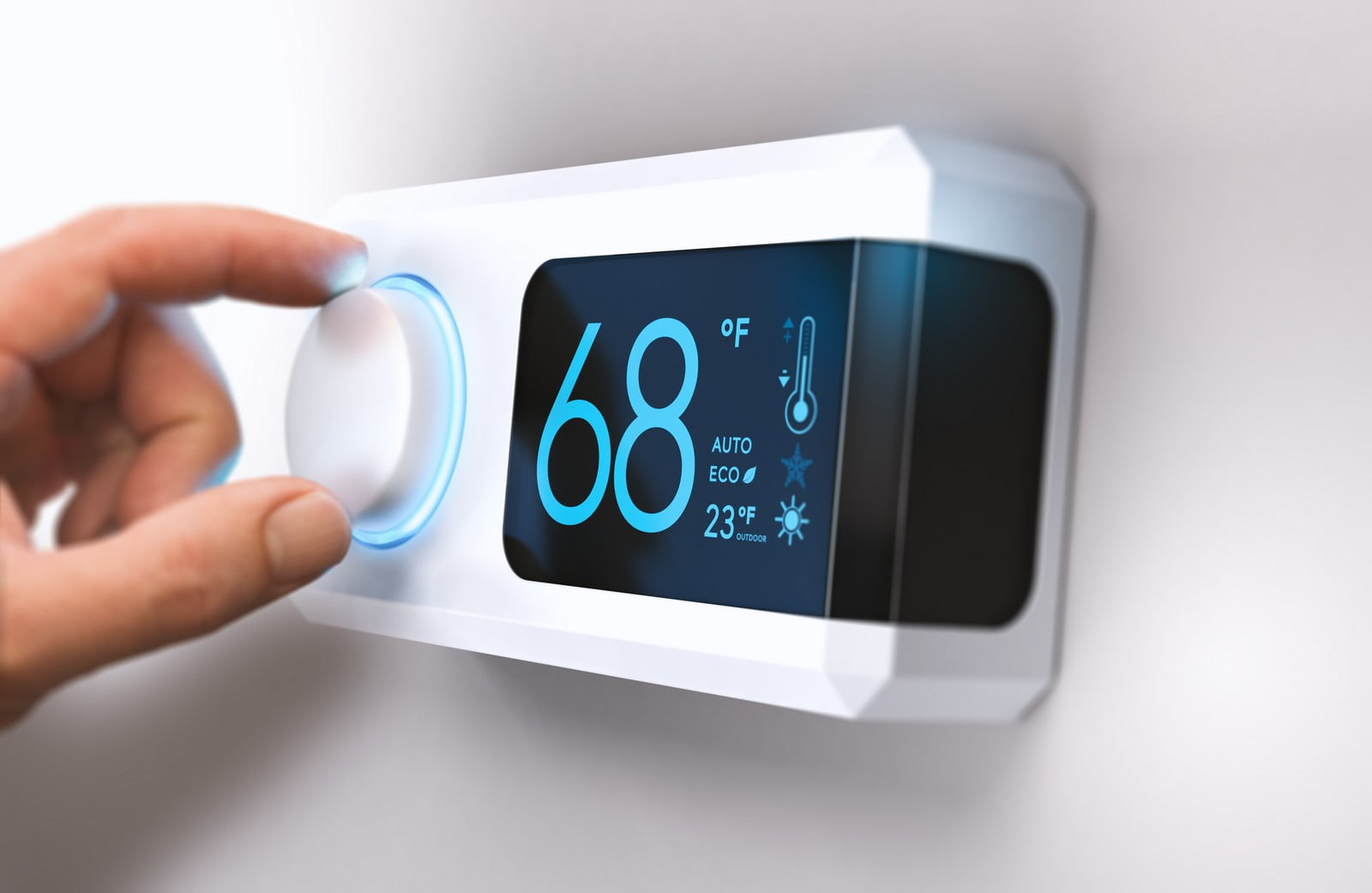 This image shows a modern, digital thermostat mounted on a wall. A person's hand is adjusting the temperature setting. The thermostat display indicates a current temperature of 68 degrees Fahrenheit and has icons suggesting that it has an automatic mode and an eco (economical/environmentally friendly) mode. Additionally, it displays an outdoor temperature of 23 degrees Fahrenheit with a snowflake icon, indicating that it's cold outside. The blue lighting around the dial and cool colour tones on the display screen add to the sleek and contemporary design of the device.