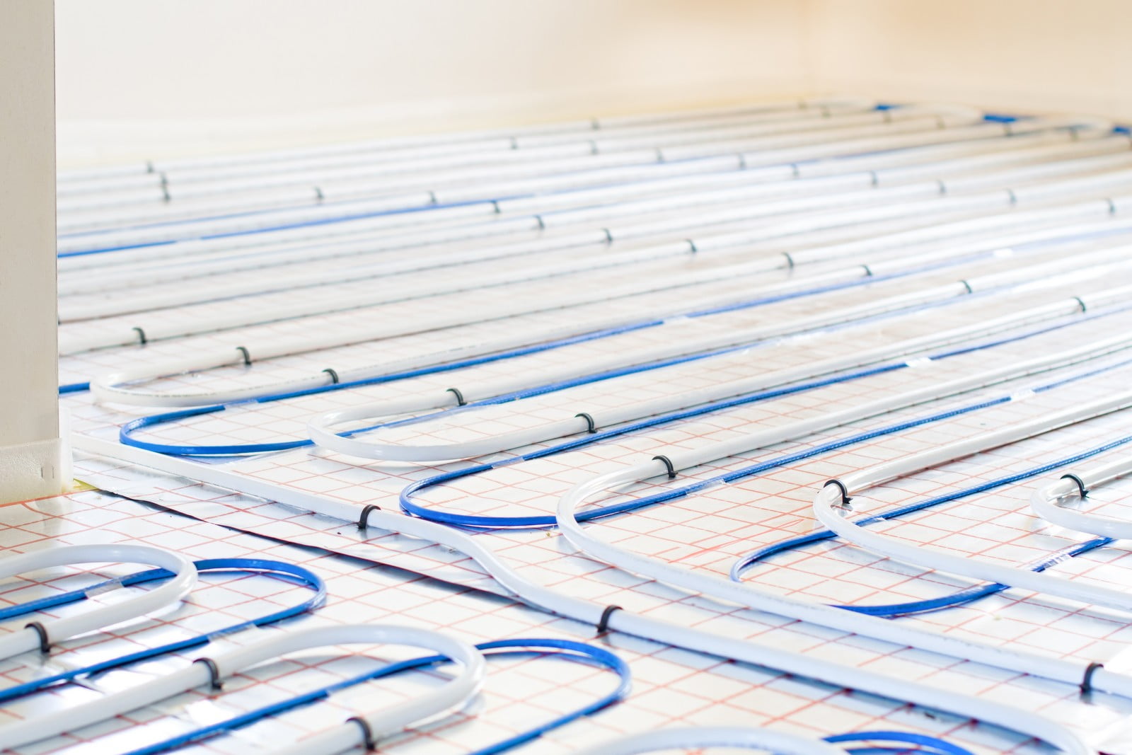 This image shows an underfloor heating system during installation. The blue pipes are laid out across the floor in a looping pattern, which will carry warm water to heat the room from below. The grid lines, likely on an underfloor heating mat or insulation board, help to ensure that the pipes are spaced evenly for consistent heat distribution across the floor. Once the installation is complete, the system is typically covered with a screed and then the final floor covering.