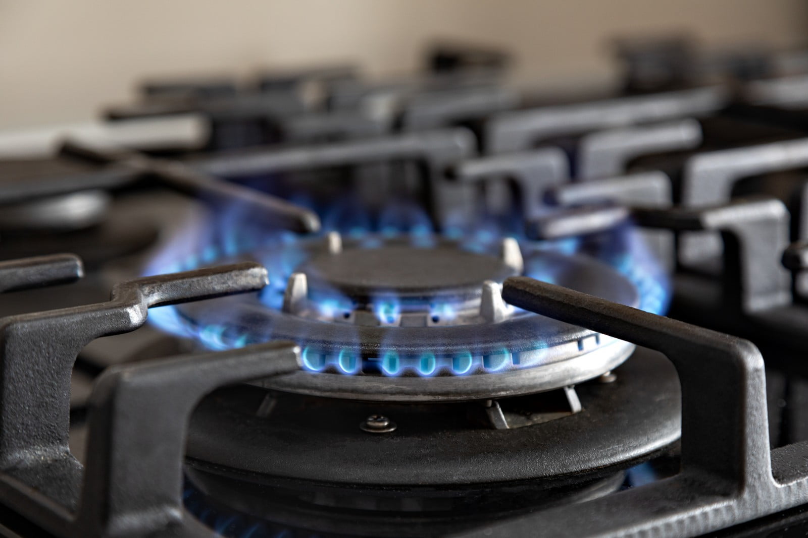 This image shows a close-up of a petrol stove burner with a blue flame, indicating that it is turned on. The burner grates, which are typically made of cast iron or another heat-resistant material, are in place to support cookware. The flame is used for cooking by providing direct heat to the bottom of pots or pans placed on top of the grate. The surrounding area of the stove is not clearly visible, but we can infer that this is a part of a kitchen setup with multiple burners.