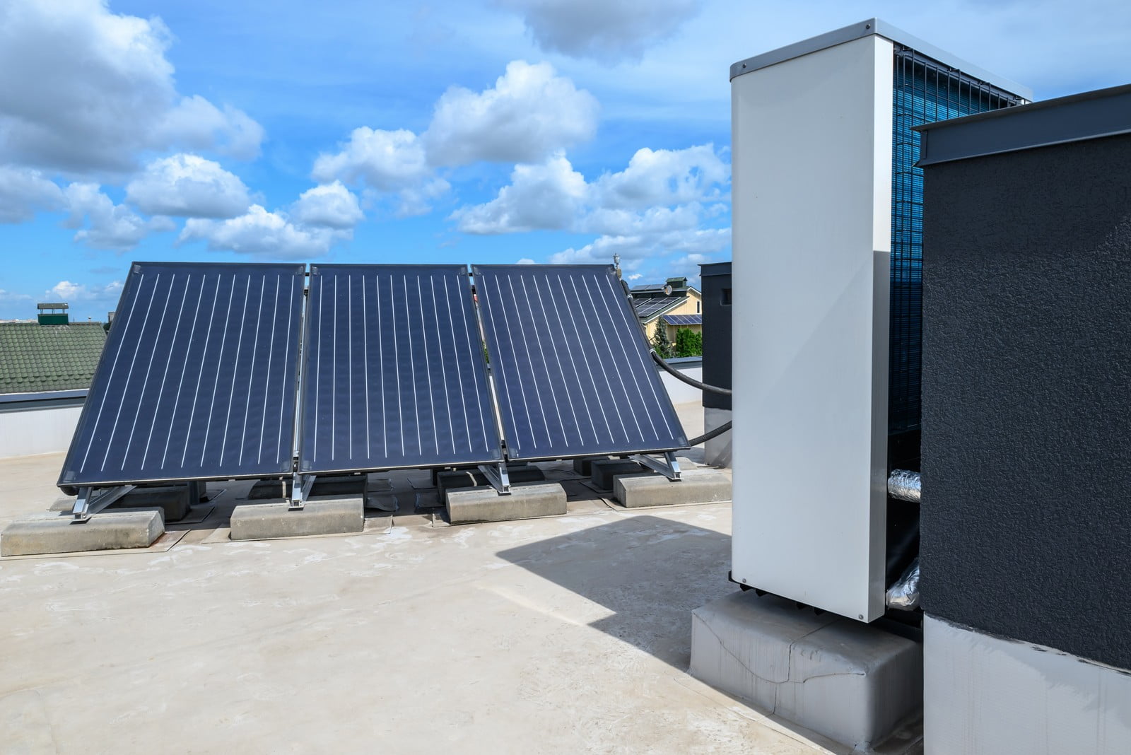 This image shows an installation of solar thermal panels on a flat rooftop. These panels are designed to absorb sunlight and use it to heat water or another fluid for residential or commercial use. You can also see various plumbing pipes and insulation related to the solar thermal system, as well as part of an HVAC (heating, ventilation, and air conditioning) unit nearby. The sky is partly cloudy, indicating that the photo was taken on a day with mixed weather.