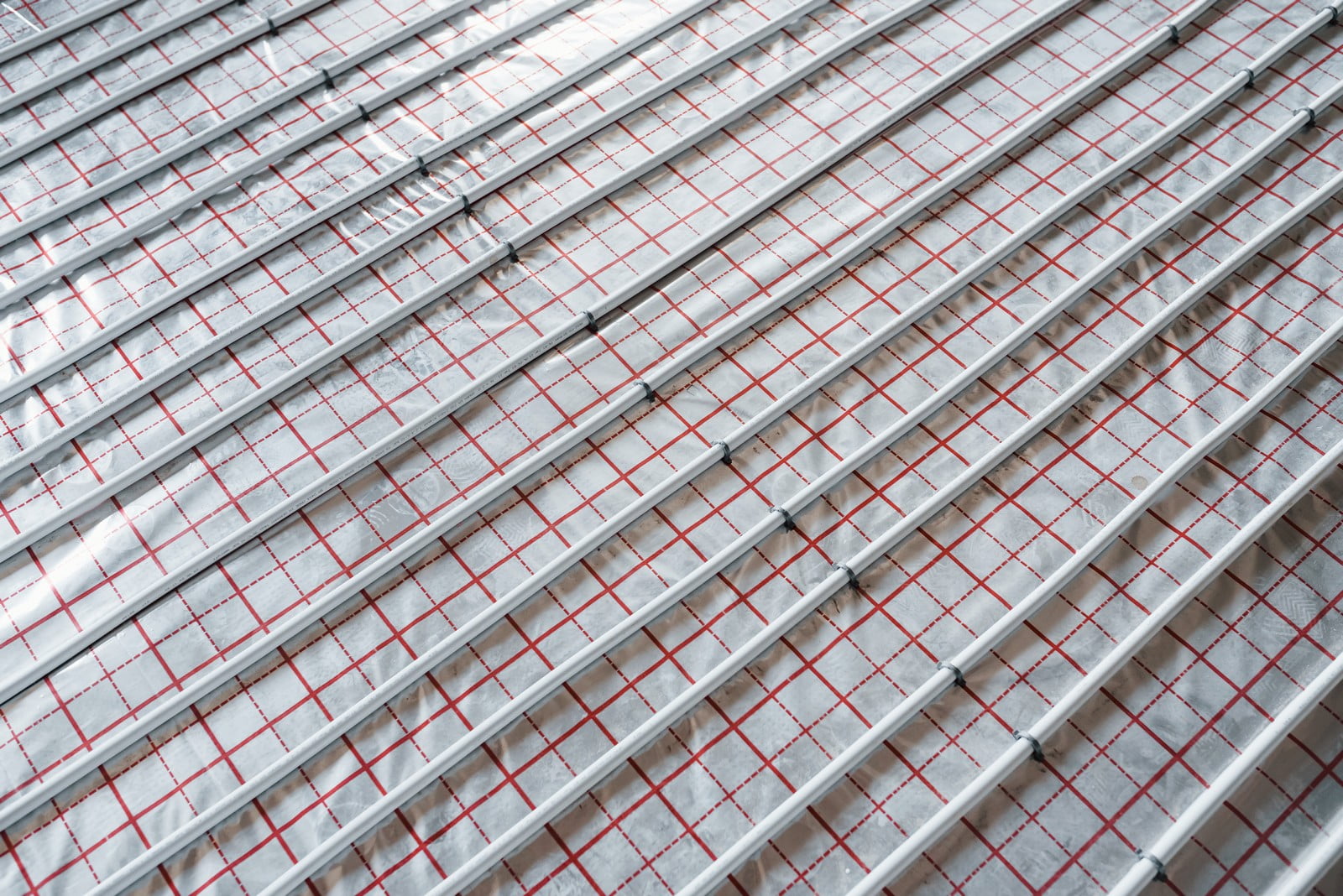 The image depicts a series of parallel metal rails or bars with a patterned surface beneath. The surface below the bars appears to be a fabric or membrane with a red grid-like pattern, possibly serving as a base layer or liner for a structure. The context suggests this could be part of a roofing system, flooring, or some other architectural feature where the bars provide support or separation from the underlying material. The specific purpose is not entirely clear without further context.